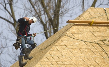 Nick Arnold of Mt. Brydges uses safety ropes and harness while climbing down a roof with a load of shingles while roofing a large home under construction just north of Sunningdale in London, Ont.  Mike Hensen/The London Free Press/Postmedia Network