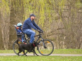 Kevin Hawkswell cycles with his 2-year-old son Jude through Gibbons Park with Leo running alongside. The parks in London are getting greener as the rain and milder temperatures coax the trees into spring in London, Ont.  Photograph taken on Tuesday April 30, 2019.  Mike Hensen/The London Free Press/Postmedia Network ORG XMIT: POS1904301532204433