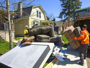 Jason Bailey hoists an armchair into a garbage truck on Huron Street in London, Ont.  Bailey and his partner Roland Sauer (left)  were kept busy loading mattresses, bed frames, couches and ottomans into the hydraulic maw of their truck.(Mike Hensen/The London Free Press)