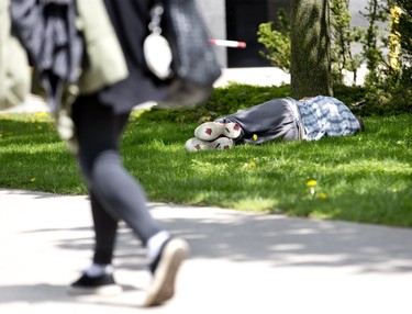A man sleeps on the grass under One London Place, the city's tallest building and a beacon of commerce in London, Ont. on Thursday May 23, 2019. Derek Ruttan/The London Free Press/Postmedia Network