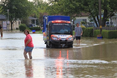 ESSEX, ONTARIO - JUNE 13, 2013 - Residents walk down a flooded street as a Windsor-Essex EMS Paramedic vehicle patrols the neighbourhood in Lucier Estates in McGregor, Ontario on June 13, 2013.   (JASON KRYK/The Windsor Star)  (SEE STORY ON UPDATED FLOOD SITUATION IN MCGREGOR)