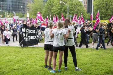 Toronto, ONT.: May 30, 2019 -- Lynn Pigeau, Lisa Hennessey, and Rebecca McLean watch a demonstration pass just after the trio arrived at Queen's Park to complete their 184 kilometre walk from London to Toronto to bring changes to corrections in Ontario. Toronto, Ont., May 30, 2019. (Nick Kozak for Postmedia News). ORG XMIT: POS1905301829450800