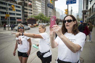 Toronto, ONT.: May 30, 2019 -- Rebecca McLean takes a photograph at Dundas Street West and University Avenue as she, Lynn Pigeau (C), and Lisa Hennessey (L) near the end of their 184 kilometre walk from London to Queen's Park to bring changes to corrections in Ontario. Toronto, Ont., May 30, 2019. (Nick Kozak for Postmedia News). ORG XMIT: POS1905301829410797