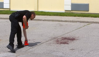 Forensic identification officer Paul Horenberg follows the blood trail that exits the Ramada Inn and ends with a large stain in the hotel parking lot after a man showed up in a London hospital with gunshot wounds Monday in London. (Mike Hensen/The London Free Press)