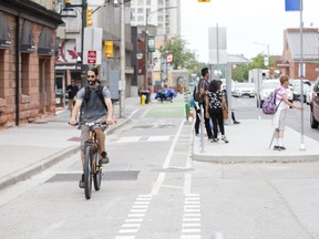 A cyclist travels along the King Street bicycle lane while others wait for the bus in London. (Derek Ruttan/The London Free Press)