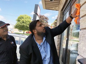 Waleed Aslam, right, wipes off the tomato sauce that was splattered on the front glass doors of the Owen Sound Muslim Association's mosque on 9th Avenue East Friday. Looking on is fellow congregation member Aziz Sameja. Denis Langlois/The Owen Sound Sun Times/Post Media Network