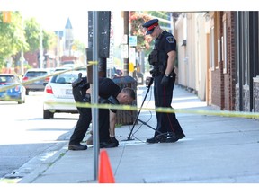 London police officers use a metal detector June 21 to search for evidence on Dundas Street, just east of English Street, following a shooting.A string of shootings in the U.S. and Toronto has increased calls for more gun control. (Free Press file photo)
