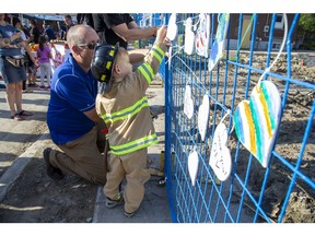 Derek Vangeffen helps two-year-old Linden Galloway hang a wooden heart he painted on a fence that surrounds homes that were damaged and destroyed by a gas explosion two weeks ago in London. Linden lives in the neighbourhood. His father Colin said that firefighters were very nice to Linden in the days that followed the explosion. As a result Linden asked to be dressed as a firefighter for Wednesday's street party and on Hallowe'en. (Derek Ruttan/The London Free Press)