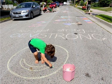 Four-year-old Bram Davis fills in a happy face on Woodman Avenue, just a few homes north of the natural gas explosion site in Old East Village in London, Ont.  Behind Davis is the slogan, "Not just strong . . . OEVSTRONG," as parents and children in the area reclaimed the closed street for themselves on Friday August 16, 2019.  (Mike Hensen/The London Free Press)