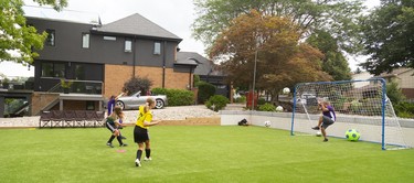 Glen Martins has to cover up as his three daughters unleash their shots simultaneously at their Byron home that features an artificial turf soccer pitch in London, Ont. Mike Hensen/The London Free Press/Postmedia Network