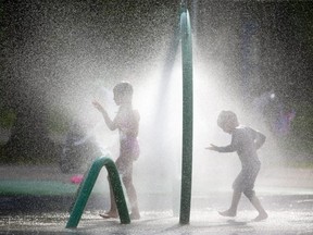 Mya Boldt, 6, and brother Kaius, 4, stroll through a sprinkler unit in the Gibbons Park splash pad late Tuesday afternoon. The heat and humidity will continue Wednesday before cooling off later in the week. (Mike Hensen/The London Free Press)