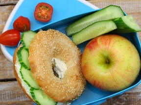 Healthy school lunch consisting of bagel with cream cheese, cucumber and apple