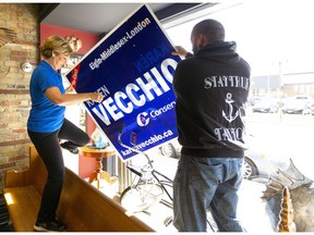 Karen Vecchio, the Conservative candidate for Elgin-Middlesex-London, steps into the window at Stay True Tattoo in London with owner Rich Lambewin to hang a campaign sign on Friday.  (Mike Hensen/The London Free Press)