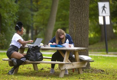 Gabrielle Williams works on her kinesiology while Kailee Dowling works on linguistics on a picnic table outside Middlesex College while enjoying the mild weather in London, Ont.  Mike Hensen/The London Free Press