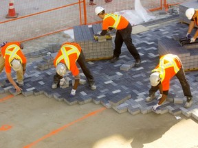 Workers from First Choice Interlock construct the river of dark stone running through the middle of the Dundas flex street in London, Ont. The bricklayers use the orange lines sprayed on the sand to map out where the darker coloured stone is laid to form the winding pattern but still have to blend in lighter stones to make it look more randomized. Mike Hensen/The London Free Press/Postmedia Network