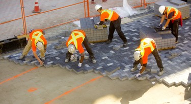 Workers from First Choice Interlock construct the river of dark stone running through the middle of the Dundas flex street in London, Ont. The bricklayers use the orange lines sprayed on the sand to map out where the darker coloured stone is laid to form the winding pattern but still have to blend in lighter stones to make it look more randomized. Mike Hensen/The London Free Press/Postmedia Network