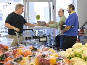 Dave Guest accepts a food bank donation bag from Len Fluhrer and Roger Khouri at the Real Canadian Superstore on Oxford Street East in London Friday. (Derek Ruttan/The London Free Press)