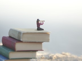 miniature woman looks at the infinity with the spyglass on a scale of books