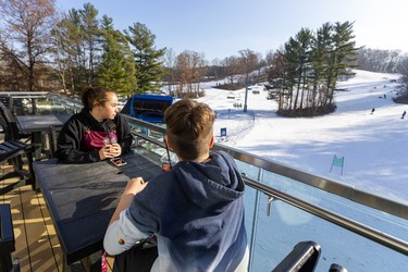 Brianna McCague, 13, and Nolan Peel, 13, both of St. Thomas, enjoy their beverages and the sunshine as they sit on the second-floor patio of the ski chalet at Boler Mountain in London. The non-profit opened their 73rd year Saturday, their earliest opening in 30 years. Mike Hensen/The London Free Press/Postmedia Network