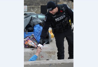 London police Const. Jeff Brown hands three pairs of socks to a man sleeping in a parking lot off of King Street on Wednesday, Nov. 6, 2019. Members of the police foot patrol unit are handing out nearly 2,000 pairs of socks collected by the London Police Assocation. (DALE CARRUTHERS / THE LONDON FREE PRESS)
