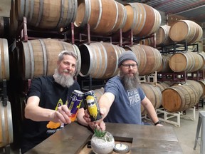 Andrew Peters, left, and Dave Reed of Forked River Brewing toast their new taproom in front of a wall of barrels filled with new beers awaiting release. (Wayne Newton/
Special to Postmedia)