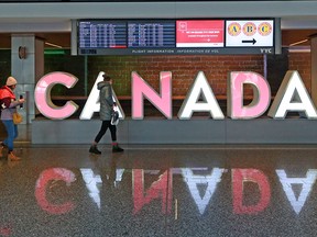 Travellers walk past the Canada sign in the International Arrivals area at Calgary International Airport on Monday, March 16, 2020. The COVID-19 pandemic has quickly reduced flights and travel around the world.