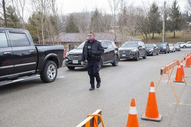 A police constable walks past line of vehicles containing people waiting to be seen by health care professionals at the  coronavirus assessment centre  now open at Oakridge Arena in London, Ont. on Tuesday.  (Derek Ruttan/The London Free Press)