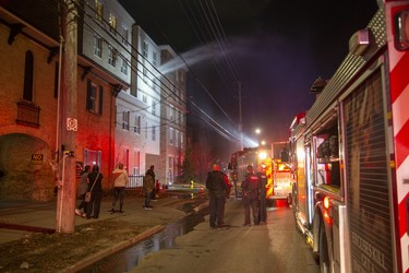 Water flies out of the window of a 4th floor apartment as firefighters dowse a fire at 446 King Street in London, Ont. on Friday March 27, 2020. One person was taken to the hospital with unknown injuries from the fire that began around 8:00pm.  Derek Ruttan/The London Free Press/Postmedia Network