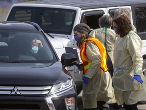 Londoners are screened in their cars for COVID-19 at the city's first assessment centre at Oakridge Arena on Monday. Occupants in a lineup of cars stretching a city block waited till they could be seen by health care workers wearing visors and masks as well as gowns. Their information was taken down and, if necessary, they were asked to park and go inside for further screening. (Mike Hensen/The London Free Press)