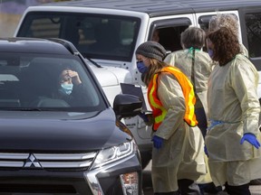 People are screened in their cars for COVID-19 at London's first assessment centre at Oakridge Arena. A lineup of cars stretching a city block waited till they could be seen by health care workers wearing visors and masks as well as gowns. Their information was taken down and if necessary they were asked to park and go inside for further screening. Photograph taken Monday March 16, 2020.  (Mike Hensen/The London Free Press)