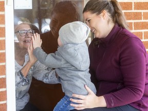 Hudson Dutot, 1, reaches out to isolated neighbour Yvonne Peckham with his mom Jenna in London on Sunday March 22, 2020.  Jenna Dutot says their neighbours Yvonne and Doug Peckham have been close friends ever since they moved onto the quiet street off of Springbank Drive. Since they can't visit anymore due to social distancing, they now come to the door to say hello. Mike Hensen/The London Free Press/Postmedia Network