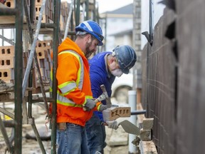 Chris Gundisch breaks off a brick as John McAboy wearing a mask applies mortar as the two men brick a wall of a home going up north of Sunningdale by Hyde Park Road.  (Mike Hensen/The London Free Press)