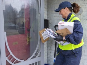Christine Billingsley, a letter carrier for Canada Post carries parcels for delivery on her route on Thursday.  Due to people being isolated, more people are shopping on line causing an increase in parcel delivery. (Mike Hensen/The London Free Press)