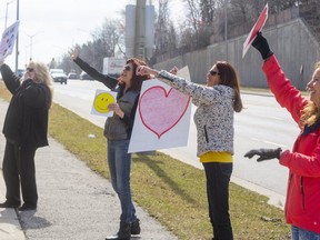 Four sisters, Wendy Van Luyk, left, Mya Van Luyk, Diana Vestering, and Nancy Joyal wave and hold signs of love for their dad, Art Van Luyk, and notes of thanks to the staff at Earl's Court Village on Highbury Avenue in London, Ont. on Friday March 27, 2020.  (Mike Hensen/The London Free Press)