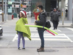 A man wearing a face mask uses foam water noodles to keep people at a distance at Yonge and Dundas Sts. on Tuesday March 17, 2020. Jack Boland/Toronto Sun