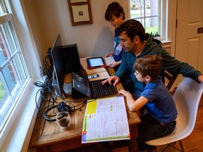 A dad helps his sons with their online home-schooling assignments in Washington during the coronavirus shutdown, just one of many tasks workers never expected they would be doing only a few week ago. (Eric Baradat/AFP)