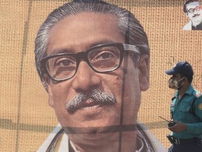 In this file photo taken on March 9, 2020 a policeman wearing a facemask amid fears of the spread of COVID-19 novel coronavirus, walks past a banner with a picture of Bangladeshs founder Sheikh Mujibur Rahman in Dhaka. - A Bangladesh military captain sentenced to death over the 1975 assassination of the country's founding leader has been arrested after almost 25 years on the run, officials said on April 8, 2020. Sheikh Mujibur Rahman, father of current Prime Minister Sheikh Hasina, was killed along with most of his family in a military coup on August 15, 1975, nearly four years after he led Bangladesh to independence from Pakistan. (Photo by Munir UZ ZAMAN / AFP)