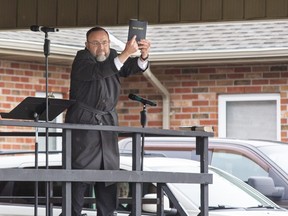 Church of God Pastor Henry Hildebrandt holds up a copy of the Holy Bible for all to see after taking the stage in the  church's parking lot in Aylmer, Ontario on Sunday April 26, 2020. In defiance of an order by the town's chief of police, the church held a drive-in service Sunday morning. Hundreds of parishioners sat in parked vehicles watching Hildebrandt on stage and listening to his sermon over their FM radios. Police video taped the event but have not yet laid charges. Derek Ruttan/The London Free Press/Postmedia Network