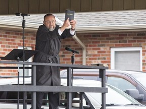 Church of God Pastor Henry Hildebrandt holds up a copy of the Holy Bible for all to see after taking the stage in the  church's parking lot in Aylmer, Ontario on Sunday April 26, 2020. (Derek Ruttan/The London Free Press)