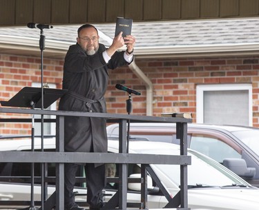 Church of God Pastor Henry Hildebrandt holds up a copy of the Holy Bible for all to see after taking the stage in the  church's parking lot in Aylmer, Ontario on Sunday April 26, 2020. In defiance of an order by the town's chief of police, the church held a drive-in service Sunday morning. Hundreds of parishioners sat in parked vehicles watching Hildebrandt on stage and listening to his sermon over their FM radios. Police video taped the event but have not yet laid charges. Derek Ruttan/The London Free Press/Postmedia Network