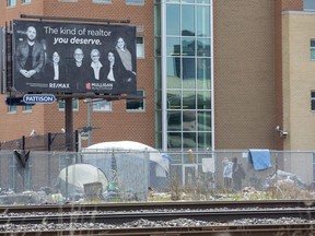 A billboard advertising a realty company looms large over a tent city where many homeless people were living beside the Salvation Army's Centre of Hope in London in April. (Derek Ruttan/The London Free Press)