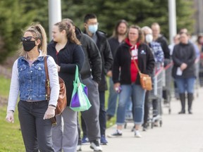 Shot with a 300-millimetre telephoto lens, people in a lineup outside a Costco in London look like they're not at a proper physical distance, but in fact the people were staying at least six feet apart (Mike Hensen/The London Free Press)