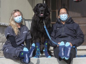 Nurse Amanda Goossens and Dr. Rod Lim, with Lim's Newfoundland Obi, all wear COVID Warrior socks that Lim designed and ordered to brighten the mood in his hospital department. The socks are now being sold by Collins Formal Wear with some of proceeds going to front-line workers.  (Mike Hensen/The London Free Press)