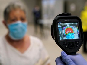 A member of the voluntary ambulance service organisation DYA (Detente y Ayuda) uses a thermal imaging camera to take the temperature of a train passenger, as half of Spain enters 'Phase 1' with the easing of one of Europe's strictest coronavirus disease (COVID-19) lockdowns, in Bilbao, Spain, May 11, 2020.