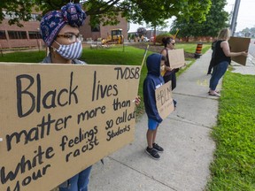 Chloe Ngakosso, 15, left, and her little sister Mabel, 10, protest with friends and family outside the Thames Valley District school board building in London. Ngakosso, a Parkside Collegiate student in St. Thomas, said she's been called the n-word at the school, while her sister also gets abusive language thrown at her. (Mike Hensen/The London Free Press)