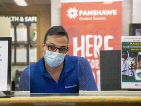 Residence services representative Moe Asmar sits behind plexiglass at the front desk of Falcon Hall, one of Fanshawe College's residence buildings in London. (Derek Ruttan/The London Free Press)