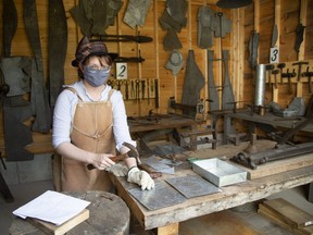 Tinsmith Christina Van Hardeveld wears a facial mask to guard against COVID-19 as she works at Fanshawe Pioneer Village in London, where precautions against the 21st-century pandemic have added a new look to the period costumes worn by staff at the 19th-century farming village. (Derek Ruttan/The London Free Press)