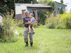 Pierre George carries his two-year-old grandson Watson Mandoka outside Pierre's home on the former army base in Ipperwash. His brother, unarmed protester Dudley George, was shot dead by police during a clash here 25 years ago this weekend. Photo taken Aug. 28, 2020. (Derek Ruttan/The London Free Press)