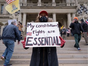 A woman wearing a face mask holds a placard as hundreds of supporters of the Michigan Conservative Coalition protest against the state's extended stay-at-home order, as the spread of the coronavirus disease (COVID-19) continues, at the Capitol building in Lansing, Michigan, U.S., April 15, 2020.