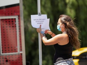 A woman places a sign reminding about social distancing on the set of the film "7th and Union" during the outbreak of the coronavirus disease (COVID-19), in Pomona, California, July 8, 2020.